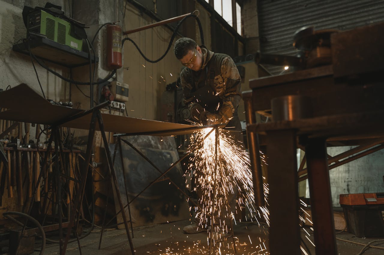 Male welder in safety gear welding metal with sparks in an industrial setting.