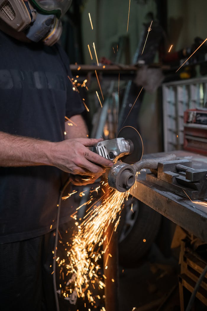 A worker using an angle grinder in a workshop, generating sparks during metal cutting.